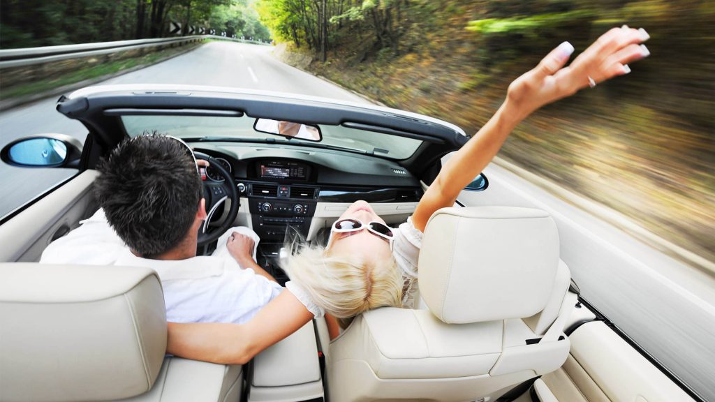 jeune couple au voulant d'une voiture cabriolet sur une route de campagne