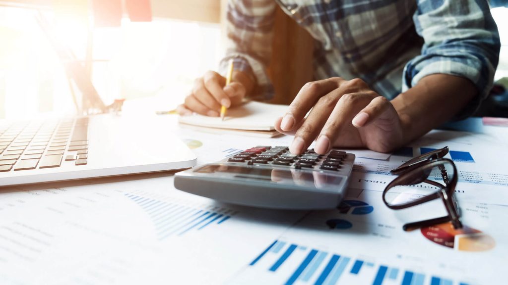 man working on calculator and computer to prepare his tax return