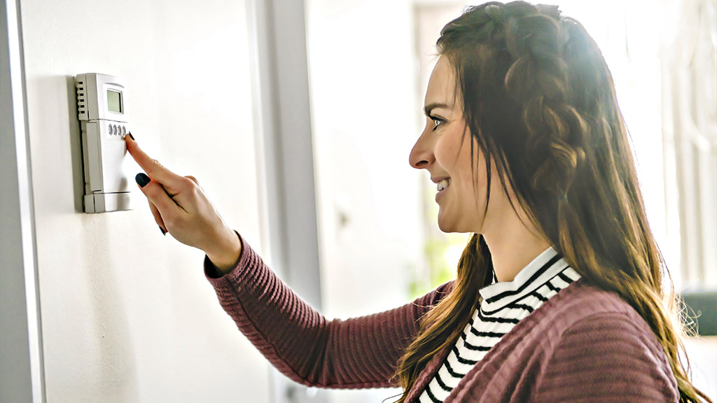 Young woman adjusting her heating thermostat.