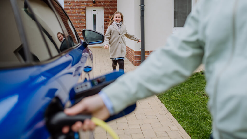 Une personne entrain de recharger sa voiture à son domicile avec un enfant qui court en arrière plan