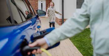 Une personne entrain de recharger sa voiture à son domicile avec un enfant qui court en arrière plan