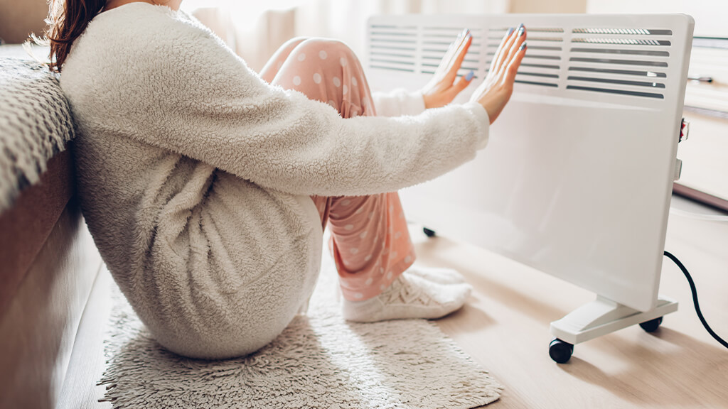 jeume femme qui  se réchauffe auprès d'un chauffage électrique d'appoint