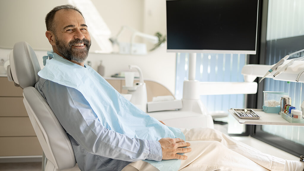Un client qui sourit assis dans un fauteuil dentaire pour sa consultation