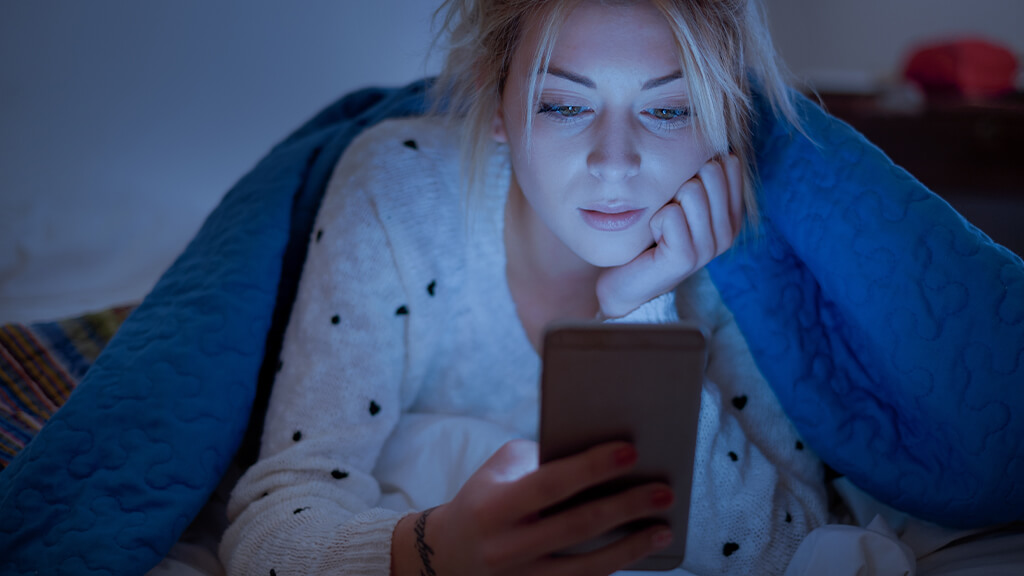 Jeune femme dans la nuit qui regarde l'écran de son smartphone