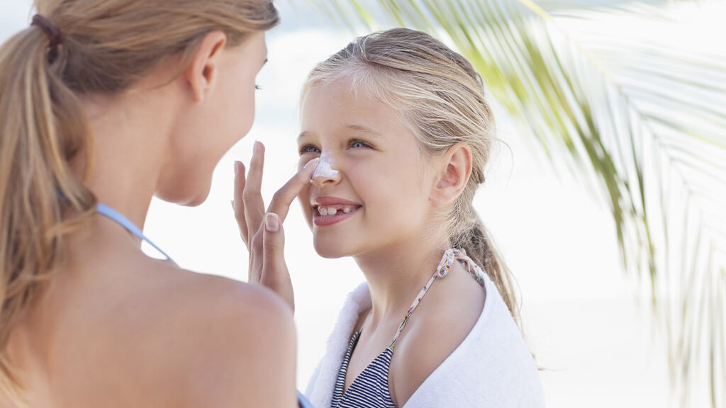 Une maman qui met de la crème solaire à  son enfant à la plage