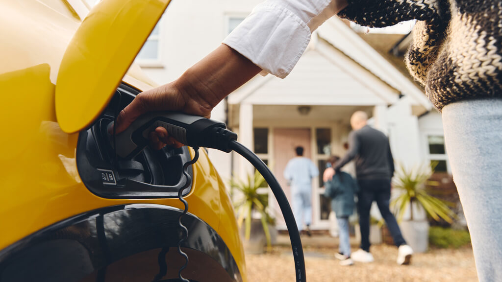 gros plan d'une personne qui recharge sa voiture électrique devant sa maison